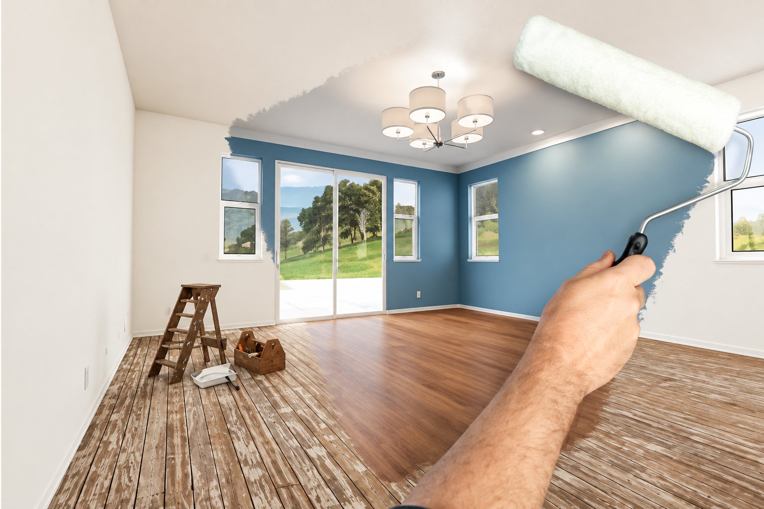 Une main tient un rouleau de peinture devant un salon lumineux dont un mur est déjà peint en bleu, avec un parquet à moitié rénové et une échelle.